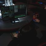 Equipe trabalha diante de computadores em uma sala escura, em atividade relacionada à segurança cibernética.