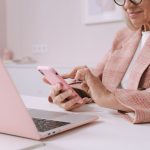 Mulher idosa usa um smartphone e um laptop sentada à mesa.