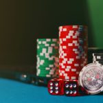 Fichas de cassino e dados sobre uma mesa, ao lado de um laptop, em referência a apostas online.