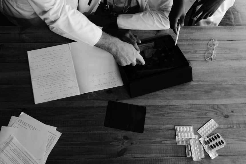 Profissionais da saúde analisam informações em tablets e cadernos durante uma atividade de pesquisa médica.
