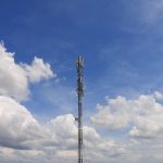 Torre de telecomunicações contra o céu azul, representando a infraestrutura das redes de comunicação.
