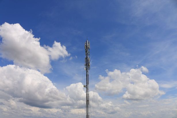 Torre de telecomunicações contra o céu azul, representando a infraestrutura das redes de comunicação.