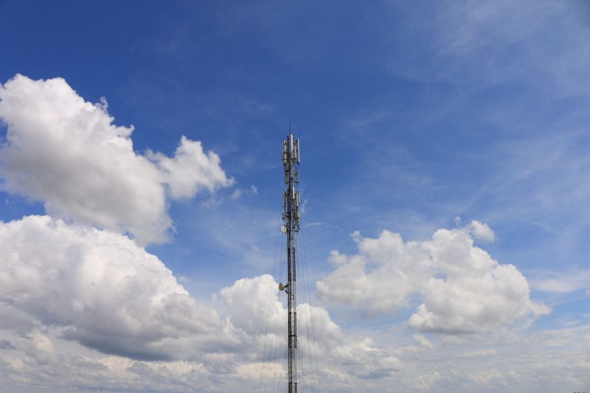 Torre de telecomunicações contra o céu azul, representando a infraestrutura das redes de comunicação.